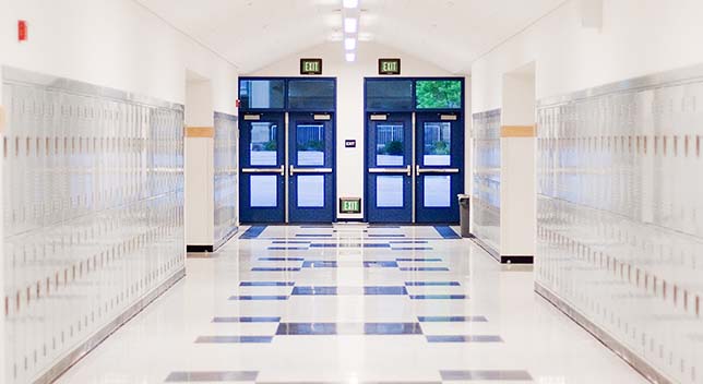 A bright white high school hallway lined with clean white lockers with two sets of vivid blue doors at the end