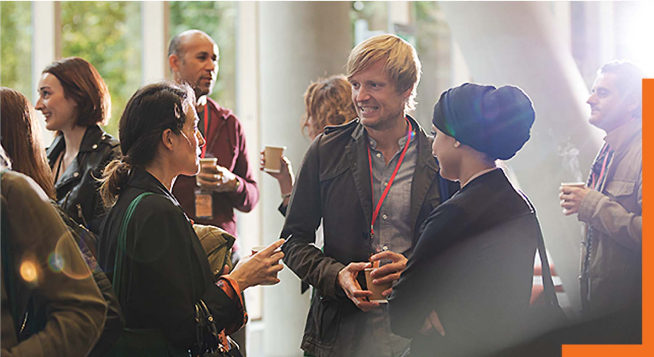 Groups of people standing together, holding beverages, and talking to each other in a sunlight-filled indoor area