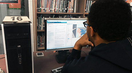 Uno studente che utilizza una postazione computer desktop per accedere a una mappa digitale e ai dati in una biblioteca scolastica