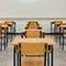 A photo of an empty sunlit classroom with clean white walls and floors, simple wooden desks, and a large blank whiteboard