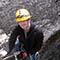 Two smiling students in safety gear rappelling down a rocky wall into a vertical cave