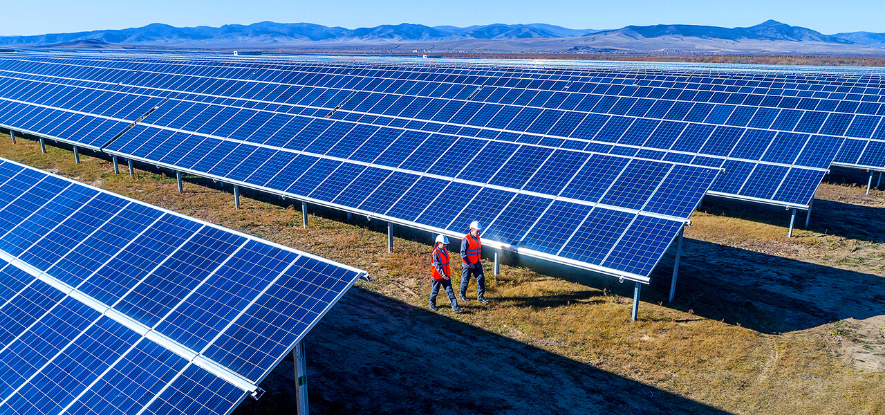Two field workers in red safety jackets walking through a field of solar panels