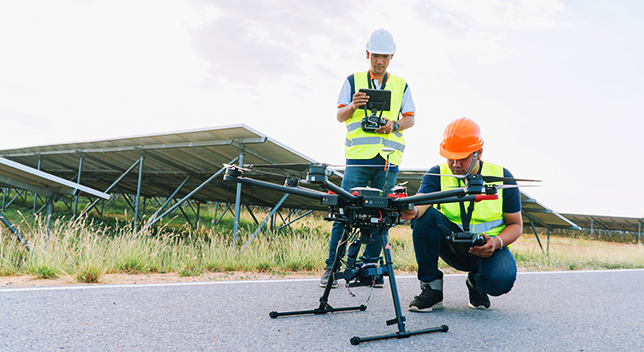 Two field workers wearing vests and hard hats working on launching a drone off the ground