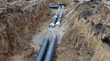 Zwei parallel verlaufende schwarze Pipelines in einem offenen Graben überlagert mit einer Wiedergabeschaltfläche