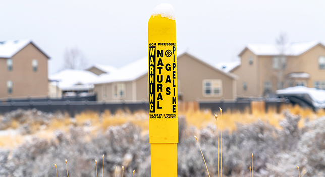 Ein gelbes Warnzeichen an einer Erdgas-Pipeline mit Schnee darauf vor einem Wohngebiet