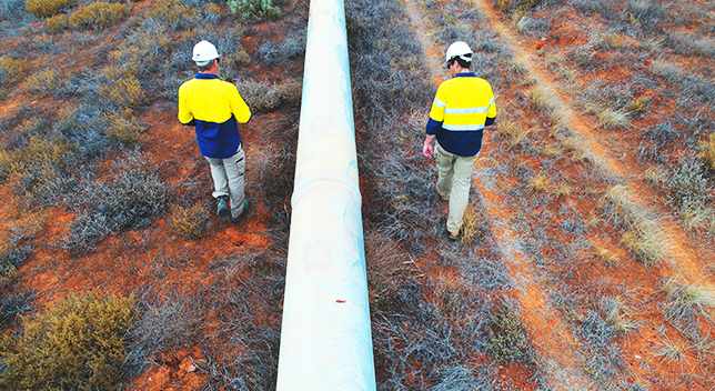 Two pipeline operators walking in a field inspecting a pipeline