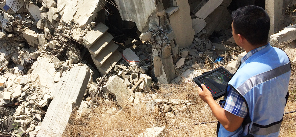 A person holding a tablet making assessments about a destroyed structure