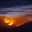 Rolling hillsides covered in a glowing wildfire silhouetted against a purple twilight sky