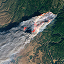 Aerial image of a smoking wildfire covering a green mountainside 