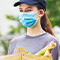 A person in a baseball cap and a mask handing a box of bananas and other food to someone else