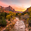 A small river rushing through a red canyon filled with green brush under a sunset sky