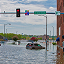 A flooded town street corner with brick buildings and partially submerged cars