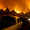 A residential street lined with cars while hills burn in the distance