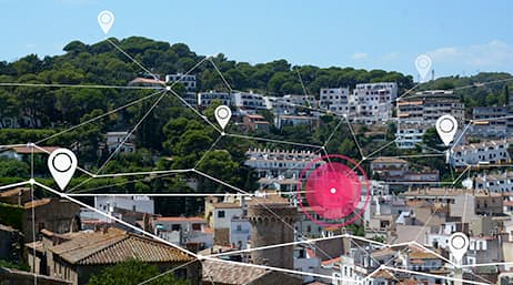 A composite image of a suburb of white and taupe houses nestled into a green wooded hillside under a clear blue sky overlaid with a computer generated network of connected white lines and map points