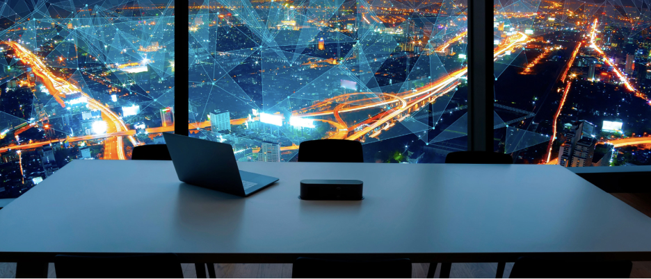 A sleek black desk with an open laptop in front of wide windows displaying a city brightly lit for night and overlaid with a network of blue webs and geometric shapes