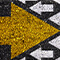 A photo of a gritty black asphalt-like surface on which is painted a large yellow arrow pointing right and many small white arrows pointing left