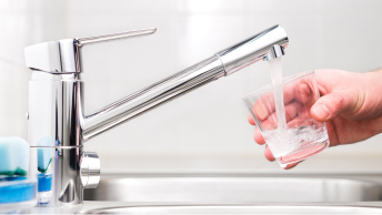 A close up photo of a hand holding a glass under a chrome water faucet 