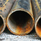 A closeup photo of a row of large black rusty pipes lying on pavement