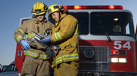 Two uniformed firefighters looking at a document together in front of a fire truck 