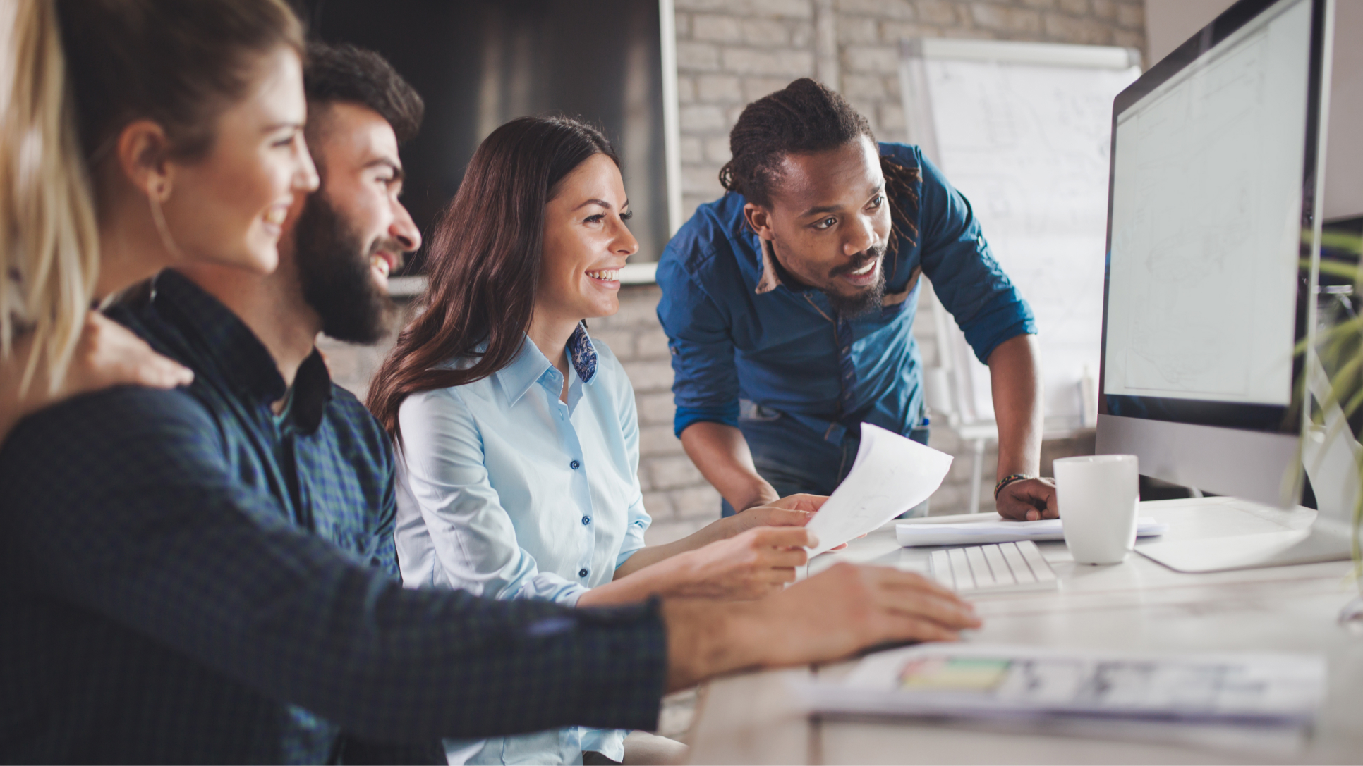 Four people looking at the same computer screen and smiling