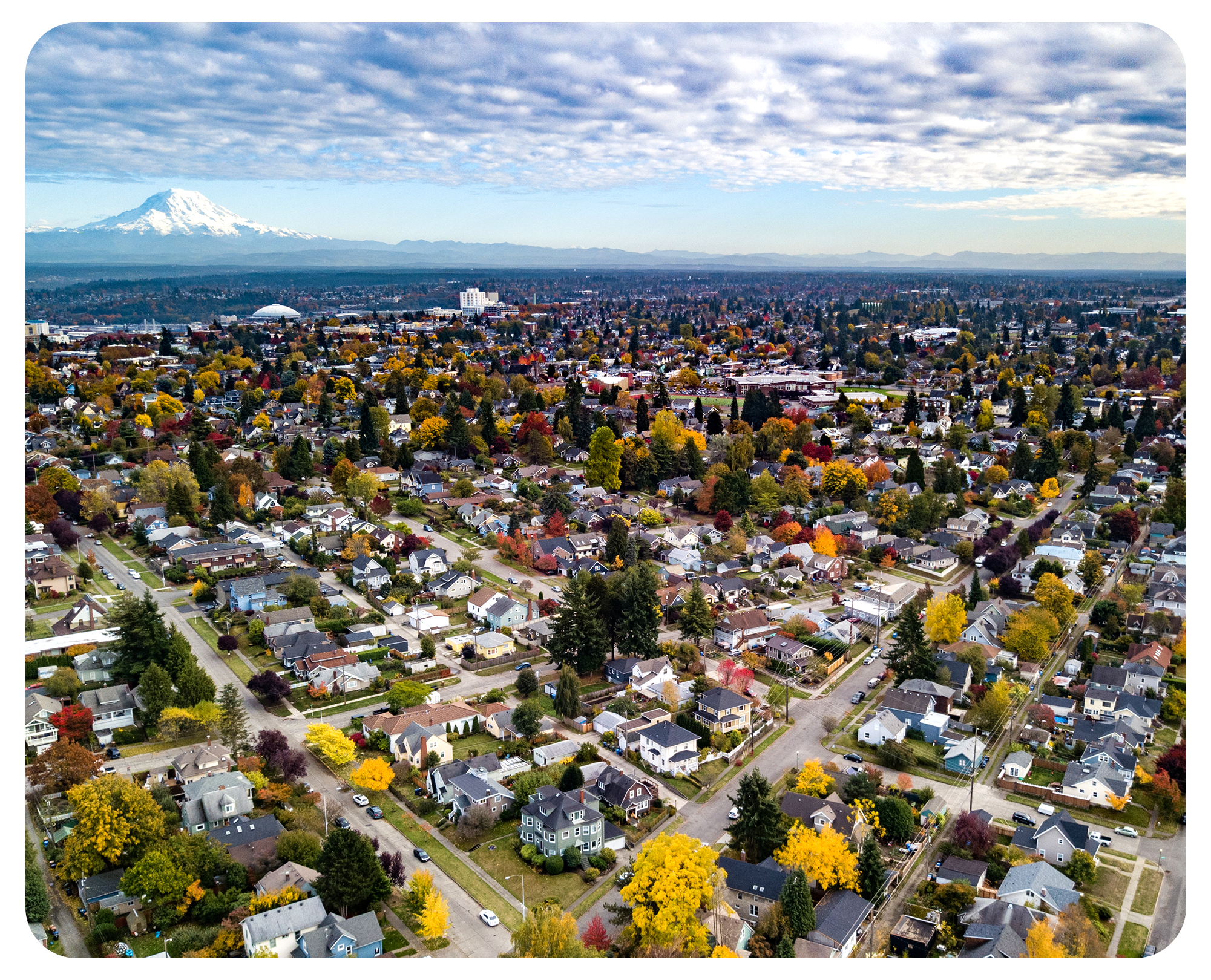 An aerial view of a neighborhood in Washington state, with Mount Rainier in the distance and a cloudy sky