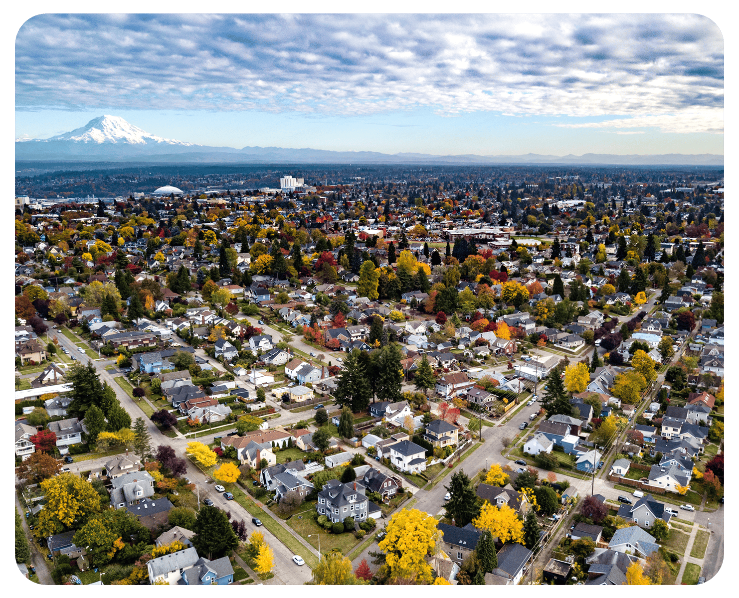 An aerial view of a neighborhood in Washington state, with Mount Rainier in the distance and a cloudy sky