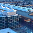 A modern airport terminal features a glass-walled building and distinctive white canopy structures on the roof. 