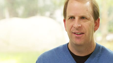 A screencap from the featured video, with Brian Cross in mid-speech wearing a blue sweater with a soft-focus sunlit meadow in the background