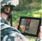 A soldier wearing camouflage tactical gear looking at a tablet displaying a data dashboard 