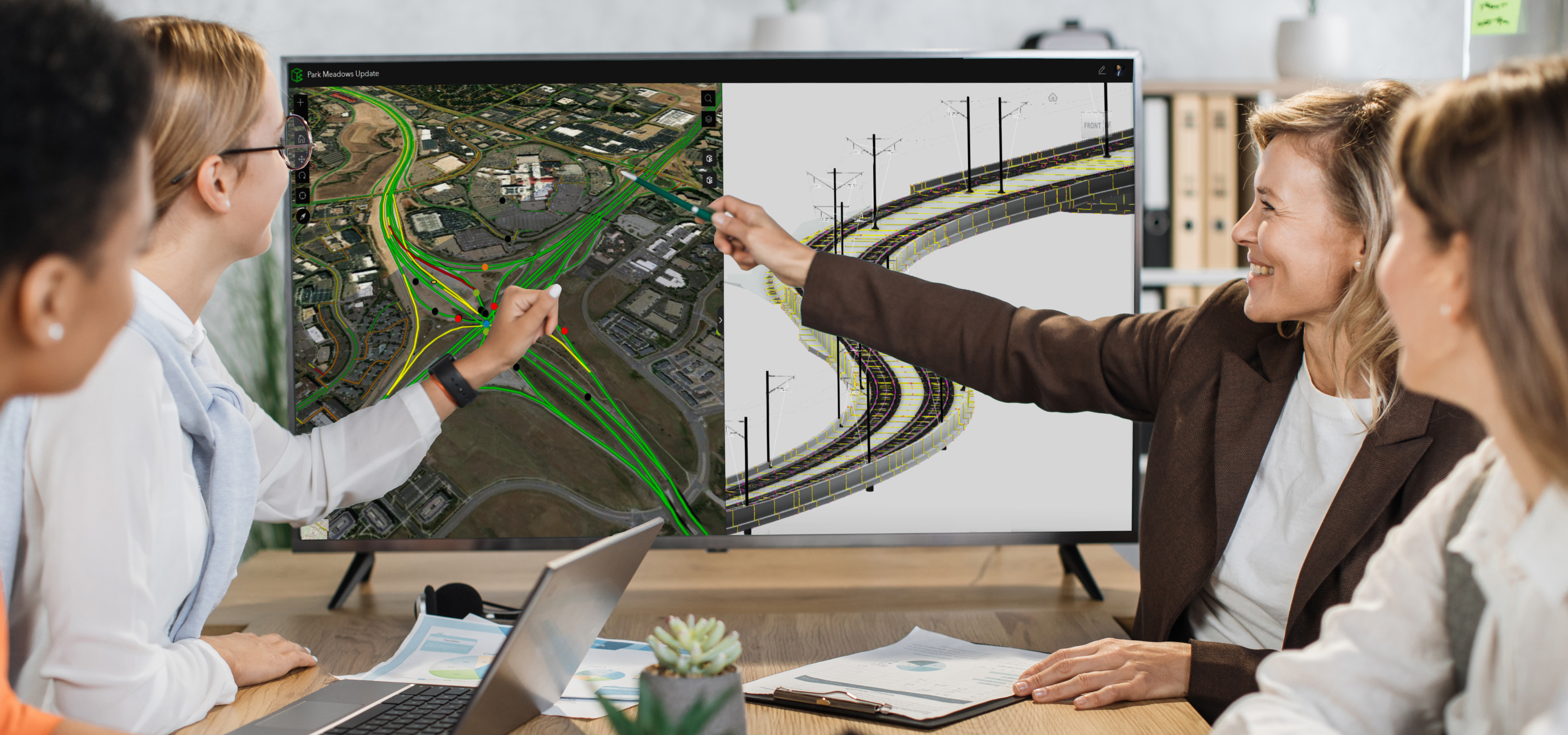 Four people sitting around a table looking at and pointing to a large screen displaying details of an infrastructure project