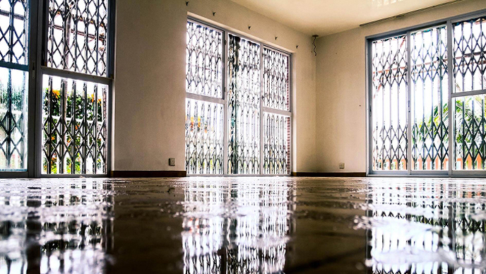 An empty, sunlit building interior with security shutters on the windows
