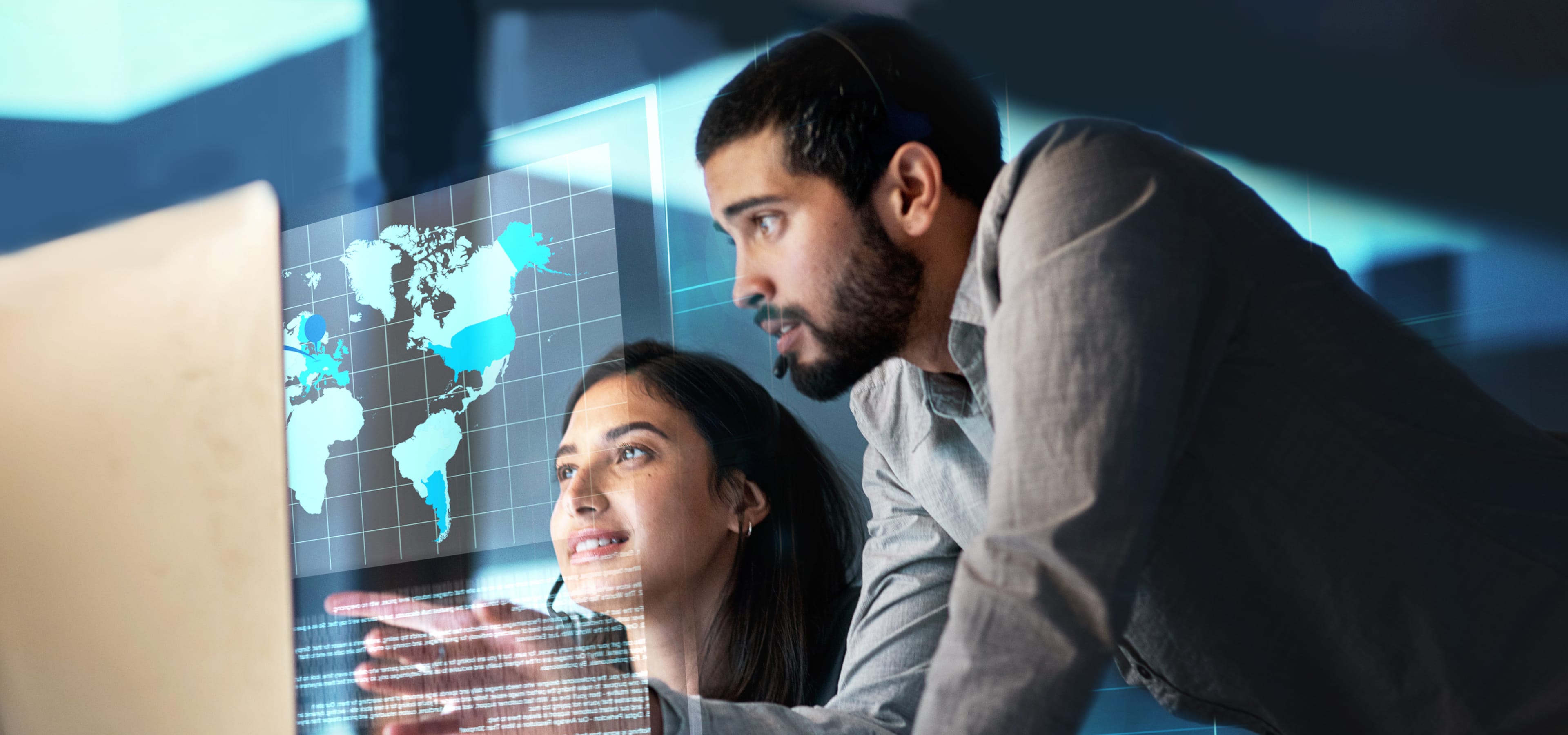 Two colleagues wearing headsets look at a computer screen with lines of code and a glowing world map in the background