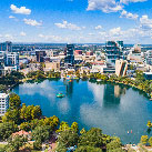 An aerial view of a clean modern tree-filled city circling a still blue lake under a vivid blue sky