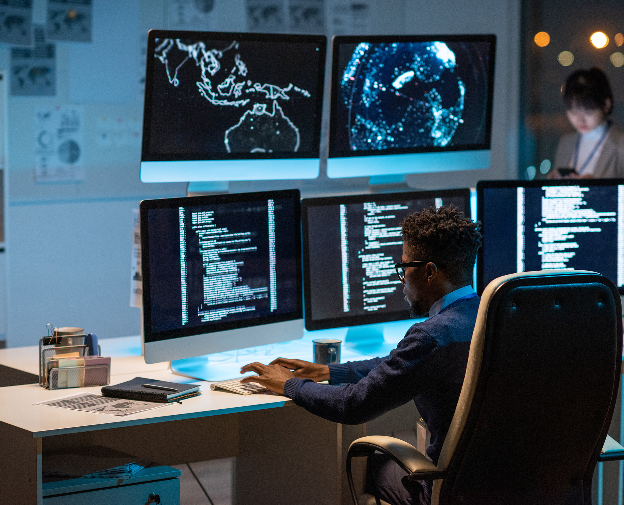 Person sitting in front of multiple computer monitors looking at maps and enterprise data. 