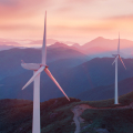 A blue mountain range dotted with white wind turbines with a vivid pink and gold sunset in the distance