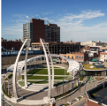 An aerial image of a modern sports complex with soaring white arches in the middle of a busy city under a clear blue sky