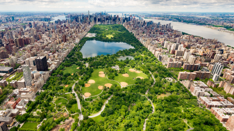 An aerial image overlooking Central Park toward downtown Manhattan shows the park in the spring with green grass and trees.