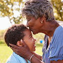 An adult kissing a child on the forehead outside on a sunny day