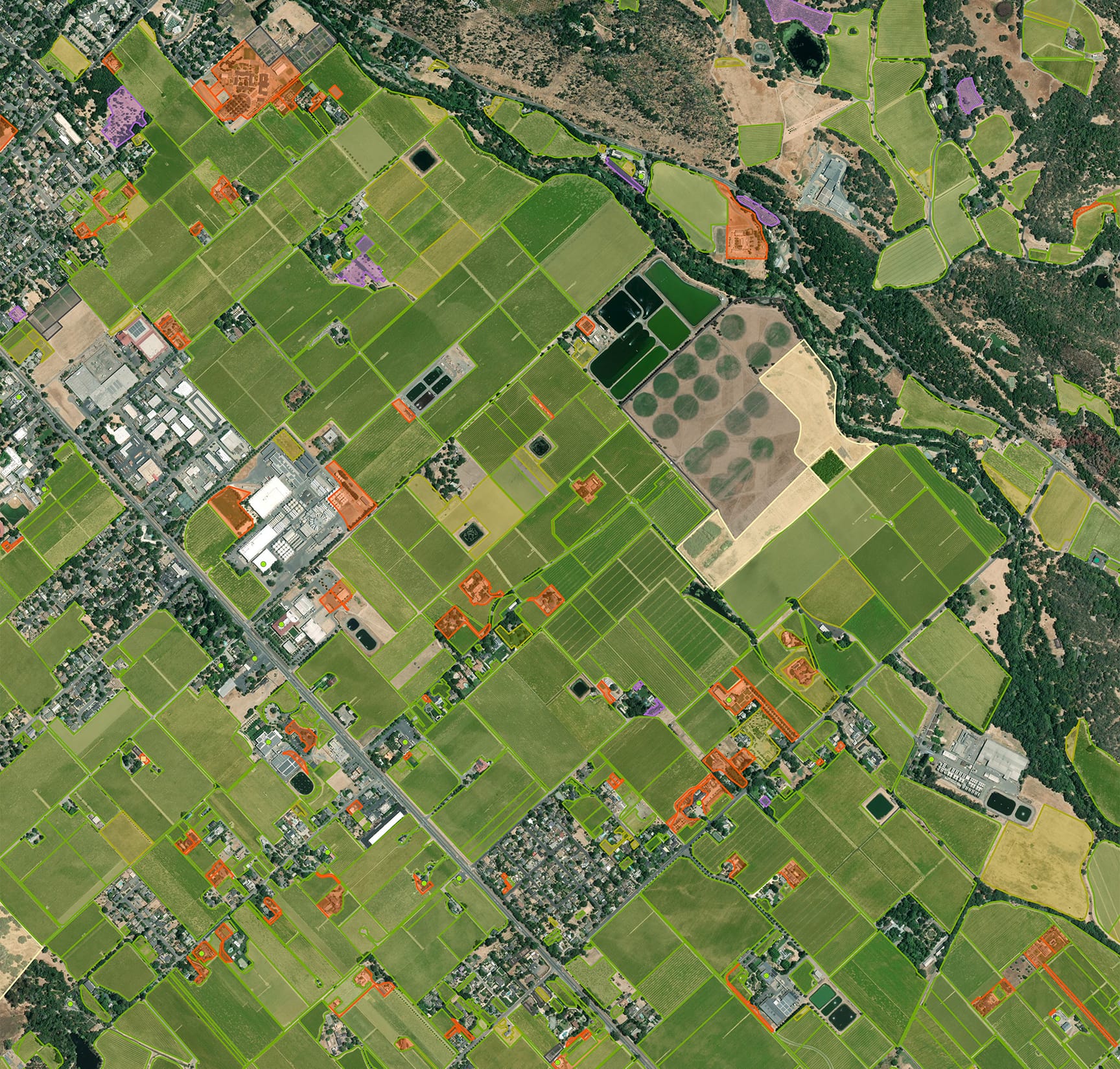 An aerial image of a region dominated by green farmland outlined in lime green polygons and some structures highlighted in orange