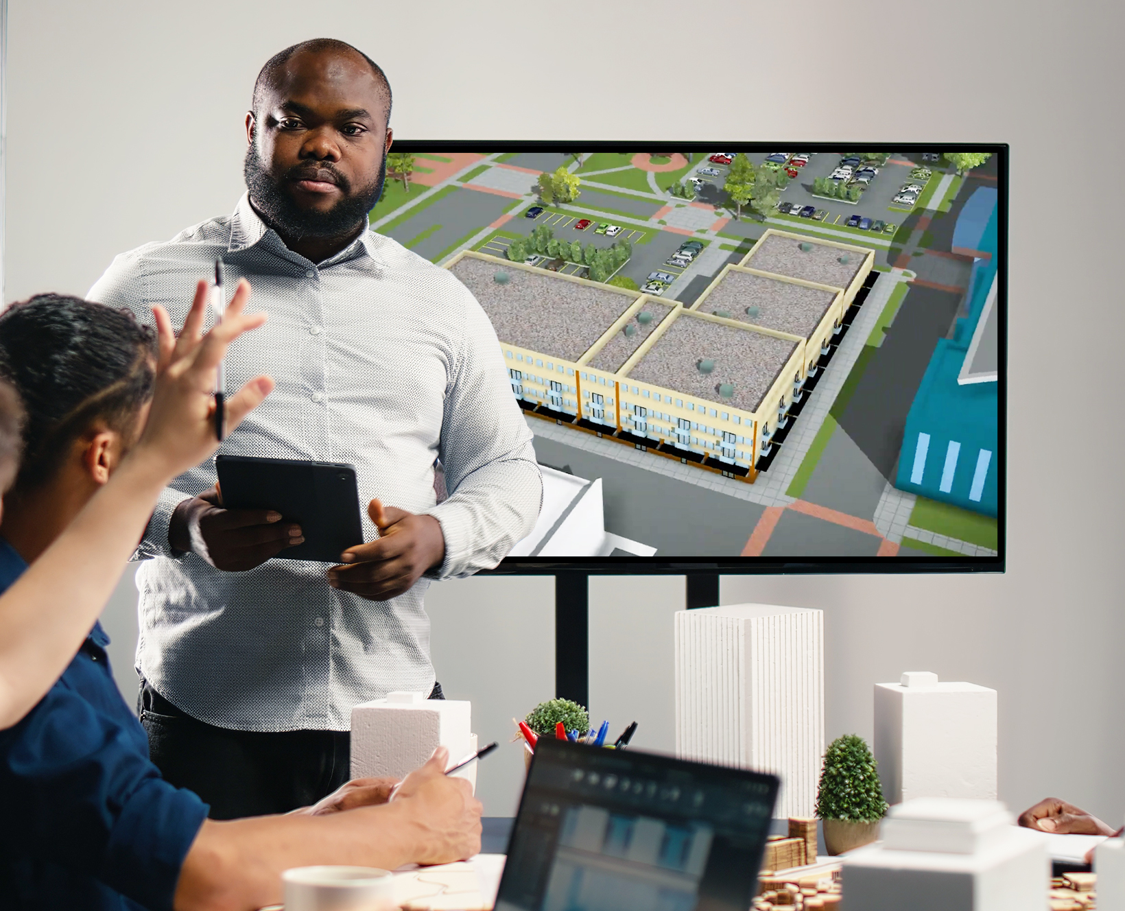 Person holding a tablet computer and talking with people about a 3D map on the screen in the room.