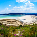 An aerial view of a large, bright blue tailings pond surrounded by mountains under a clear blue sky 