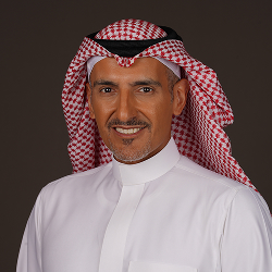 Studio portrait of a person wearing a white robe and patterned head covering against a dark background