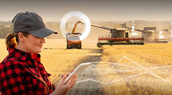 A mobile worker looking at a tablet while in front of farming tractors in the field, overlaid by statistical graphics and charts