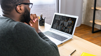 A person sitting at a table on a video call while on their laptop