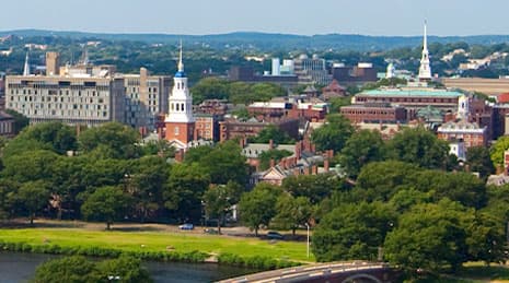A view of Harvard University’s campus, showing a lake, bridge, and trees surrounding the campus
