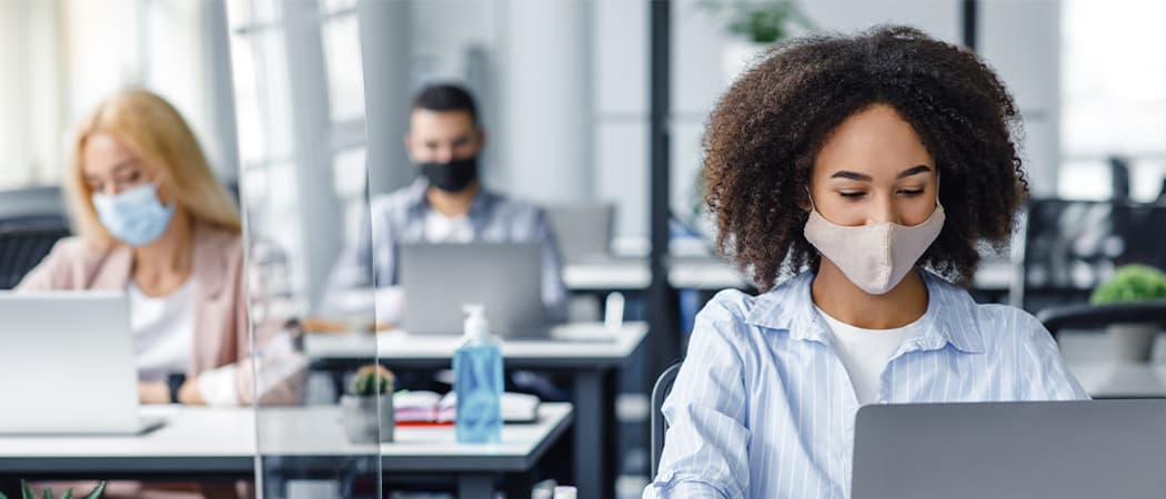 Three employees wearing masks working on laptops, seated