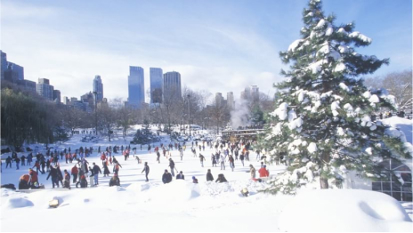 A busy outdoor ice skating rink with a city skyline in the background