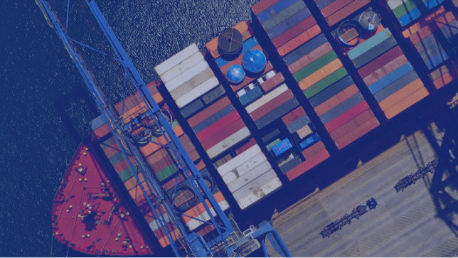An aerial view of a container ship at a dock with a crane loading containers on the bow