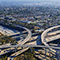 Aerial photo of a complex freeway interchange with layered overpasses in the heart of a hazy tree-filled city