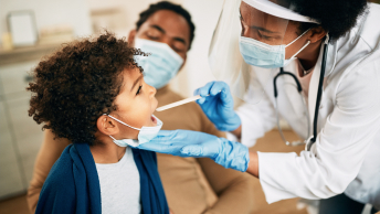 A doctor examining a child’s throat while the child sits in their parent’s lap
